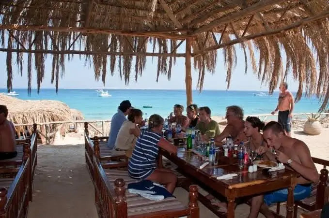 Group of people dining outdoors, representing the All-day snorkeling trip to Mahmya Island with lunch, showcasing a relaxed and social excursion atmosphere.