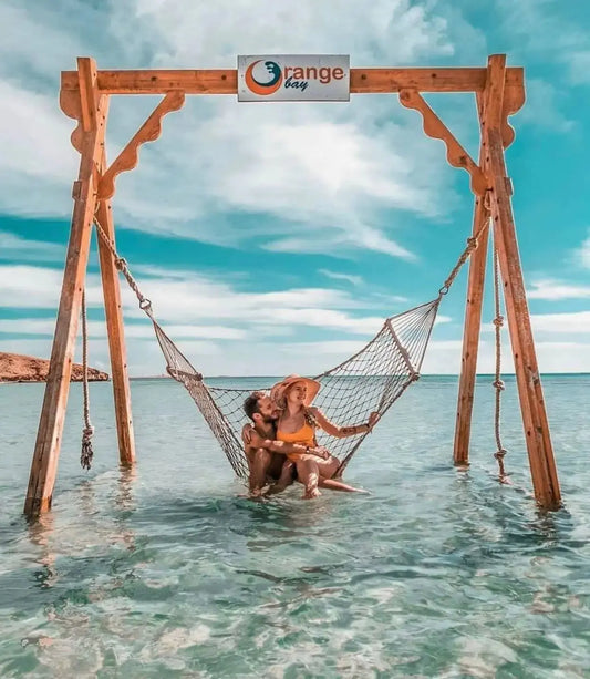 Couple relaxing in a hammock over water, part of the Orange Bay Tour, offering adventure and relaxation in Hurghada's serene beach setting.