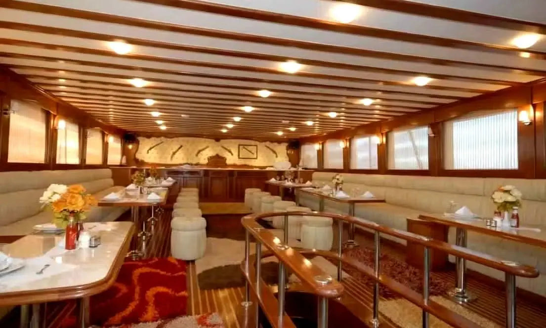 A spacious interior cabin with several rectangular tables and full-length benches in an elegant white leather look. Matching stools complete the stylish ambience. Decorative pirate pistols on the back wall set maritime accents and underline the adventurous flair.