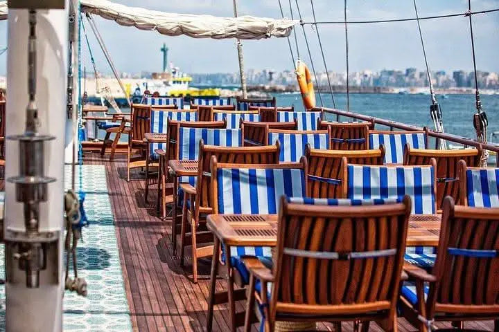 An inviting deck on a sailing boat with several rectangular wooden tables and cozy seating. The white and blue seat cushions lend a maritime atmosphere, while the abundance of wood creates a warm and inviting mood.