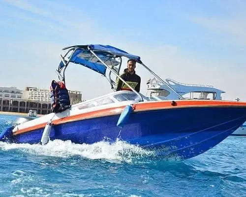 Man in a black shirt standing on a speedboat, representing the Orange Bay island private speedboat experience over the Red Sea's sparkling waters.