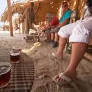 People enjoying 3-hour Safari with Quad-Bike and Camel Ride, depicted with beach elements, emphasizing adventure and cultural experience in desert landscape.