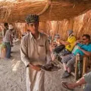 Man holding food tray, surrounded by people, visually representing the adventurous 3 hour safari with quad bike and camel ride experience in a social setting.