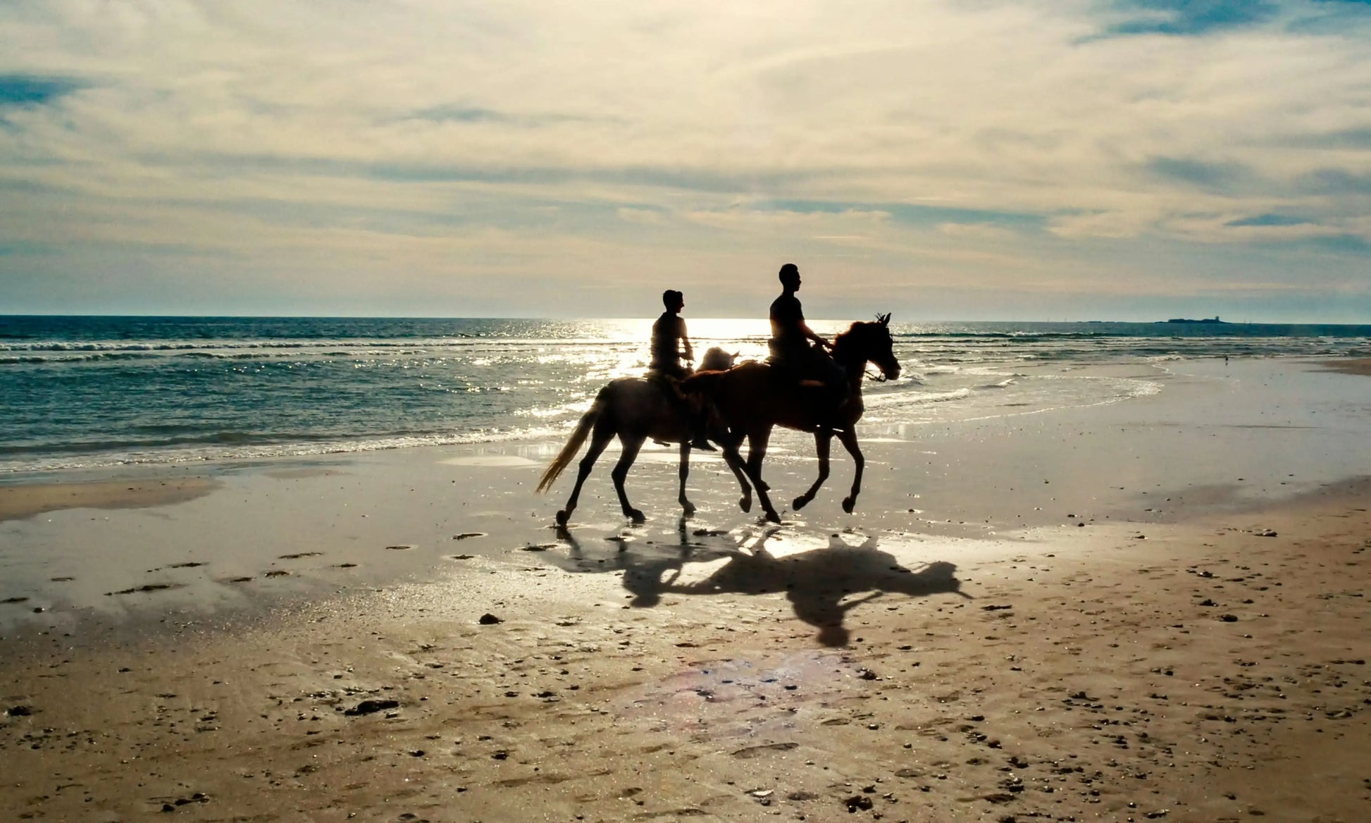 Two people are riding horses on a beach, representing the horse-riding (3 hours) experience, offering serene coastal and desert horseback adventures.