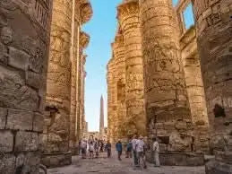 Group exploring ancient ruins with stone pillars under a blue sky, part of the day trip to Luxor, highlighting historical sites like Karnak Temple and the Valley of the Kings.