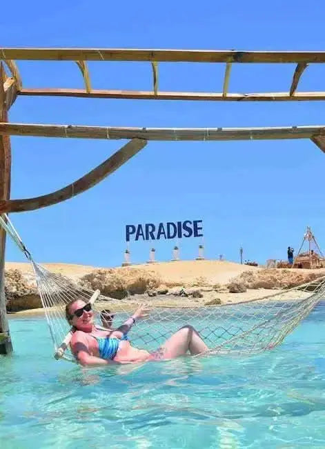 Woman relaxing in hammock over water, illustrating the Paradise Island with private speedboat and snorkeling experience, showcasing leisure and adventure.