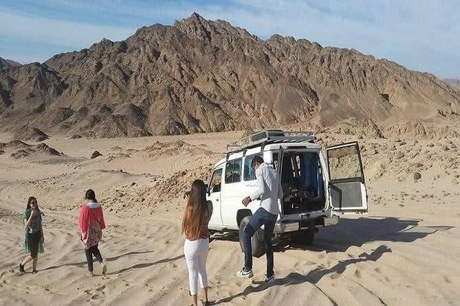 A group in the desert near a van, part of the Jeep-Safari with Stargazing experience in El Gouna, featuring camel rides and Bedouin cultural activities.