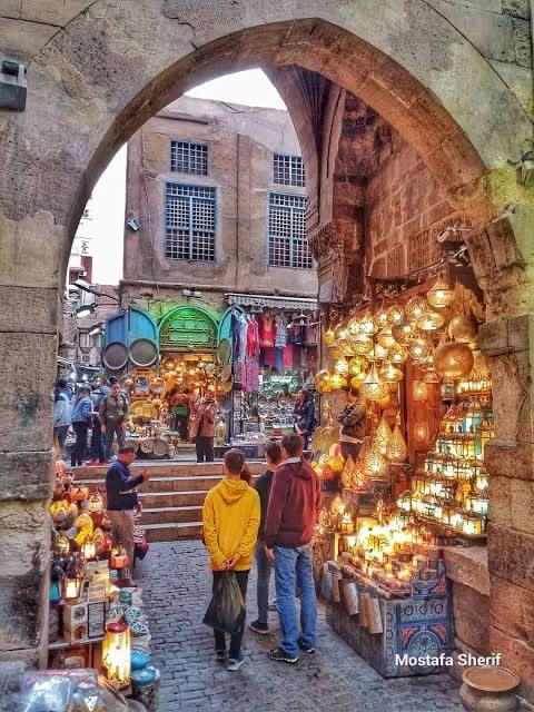 Cultural tour to Cairo - 1 day: People exploring a vibrant street market near a stone archway, highlighting cultural immersion during the Cairo day trip.