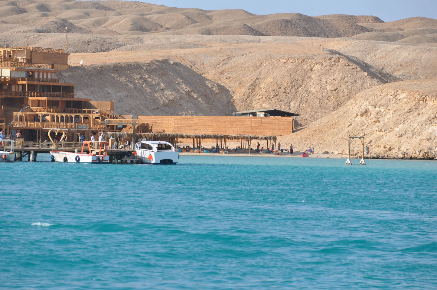 Boat on water near sandy hills, part of the Orange Bay Tour in Hurghada, offering snorkeling, beach relaxation, and watersports.