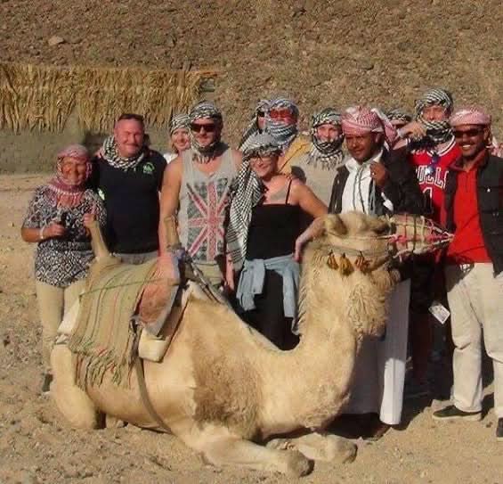 Group posing with a camel during the jeep safari with stargazing, capturing the adventure and cultural experiences offered in the desert excursion.