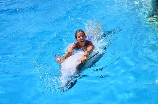 A lady swims with a dolphin in the pool. looks is pulled by it.