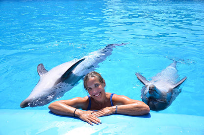 You see a lady in the pool with 2 dolphins swimming on her left and right back next to her
