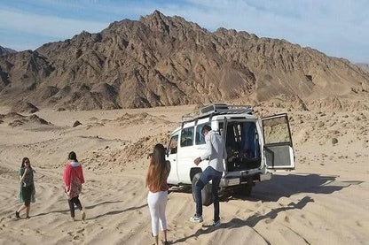 A group in the desert near a van, part of the Jeep-Safari with Stargazing experience in El Gouna, featuring camel rides and Bedouin cultural activities.