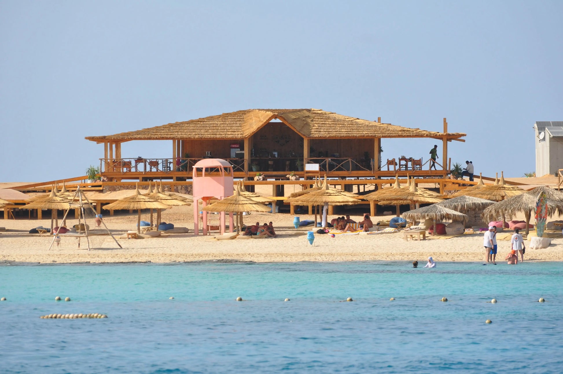 Orange Bay Tour: A scenic beach view with a building, umbrellas, and people enjoying the sandy shores, representing relaxation and adventure in Hurghada.