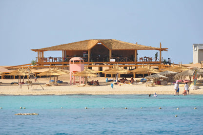 Orange Bay Tour: A scenic beach view with a building, umbrellas, and people enjoying the sandy shores, representing relaxation and adventure in Hurghada.