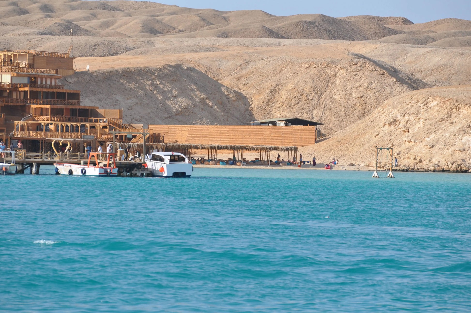 Boat on water near sandy hills, part of the Orange Bay Tour in Hurghada, offering snorkeling, beach relaxation, and watersports.