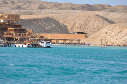 Boat on water near sandy hills, part of the Orange Bay Tour in Hurghada, offering snorkeling, beach relaxation, and watersports.
