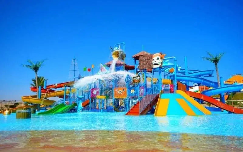 Jaz Makadi Aquaviva Waterworld featuring water slides, a pool with a red staircase, and vibrant play areas under a clear blue sky. Perfect for family fun.