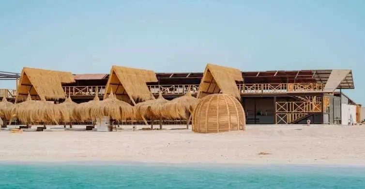 Eden Island Tour: Scenic beach with straw umbrellas and huts, capturing the serene start of an immersive snorkeling adventure in Hurghada's crystal-clear waters.