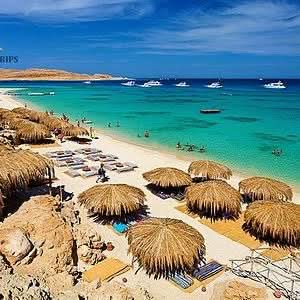 Beach scene with straw umbrellas and chairs under a sunny sky, representing the Eden Island Tour experience in Hurghada's serene coastal environment.
