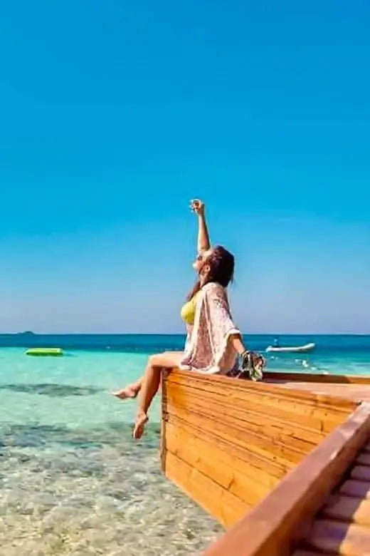 Kobieta w żółtej szacie na drewnianej balustradzie, z widokiem na ocean, symbolizująca przygodę z Eden Island Tour, ukazująca spokojne piękno Morza Czerwonego.