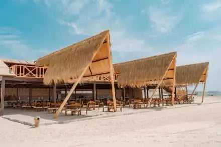 Eden Island Tour: Budynek ze strzechą i stolikami na piaszczystej plaży, podkreślający spokojną scenerię nadchodzącej przygody z nurkowaniem w Hurghadzie.